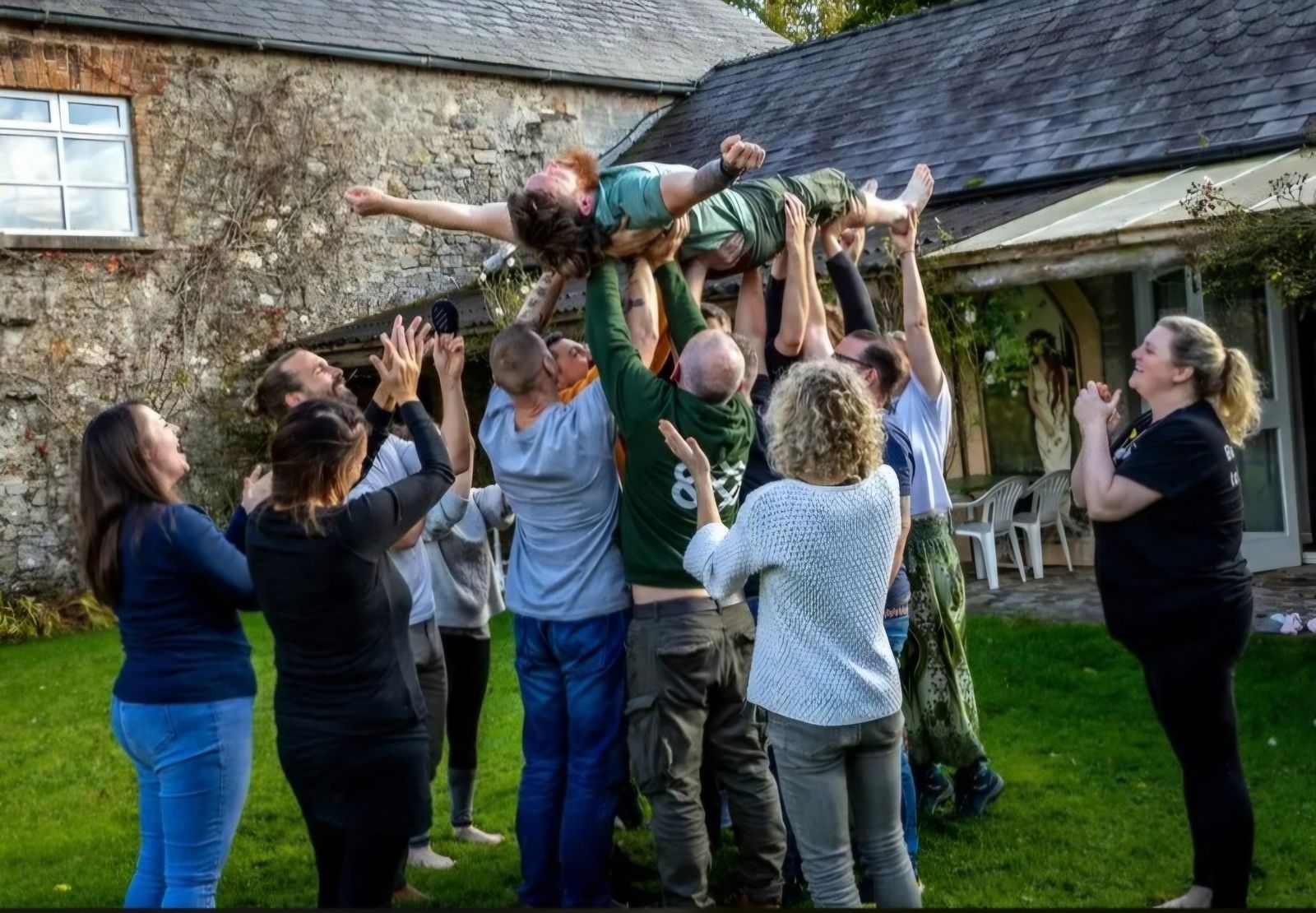 A group lifting one of the participants into the air outside a stone building