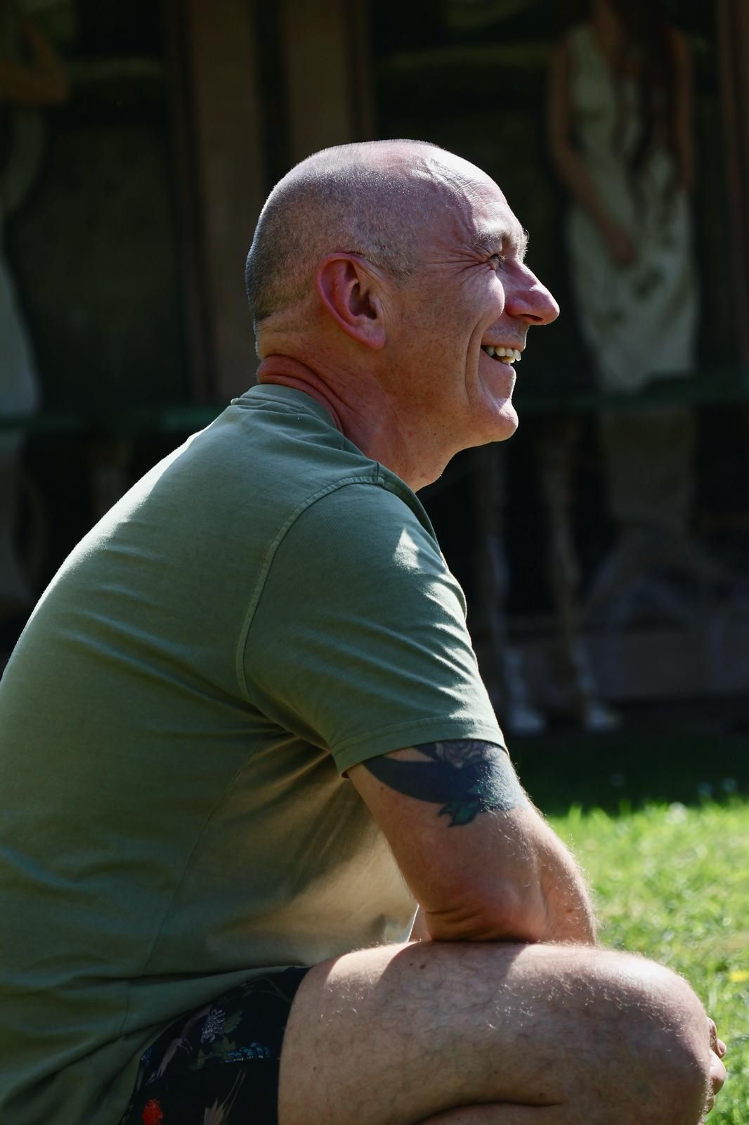 A man smiling, crouched on the grass in the sun